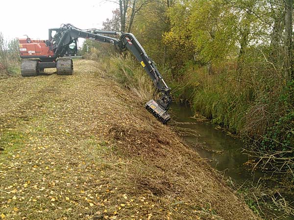 23 Tonnen-Kurzheck-Moorkettenbagger mit Forstmulcher zum Mähen einer Uferböschung mit Gehölzaustrieben 23 Tonnen-Kurzheck-Moorkettenbagger mit Forstmulcher zum Mähen einer Uferböschung mit Gehölzaustrieben
